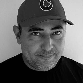 Black and white photograph of a man looking directly at the camera. He is slightly smiling and cleanly-shaven. He wears a cap. 