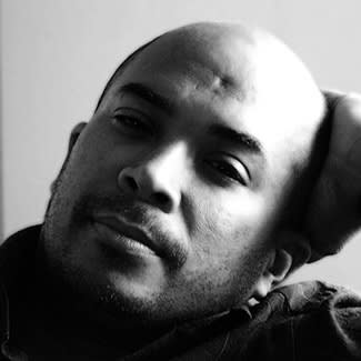 Black and White photograph of artist Armando marino. He is bald, lightly bearded and rests his hand against his hand. He looks to be between early and mid-thirties.