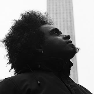 Black and white photograph of a man in profile with an afro looking up to towards the sky. 