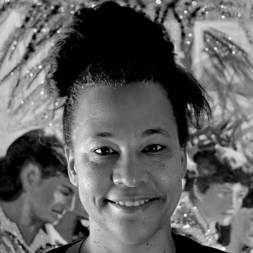 Black and white photo of a smiling woman looking directly at the camera. He hair is tied in a bun that sits atop her head. 
